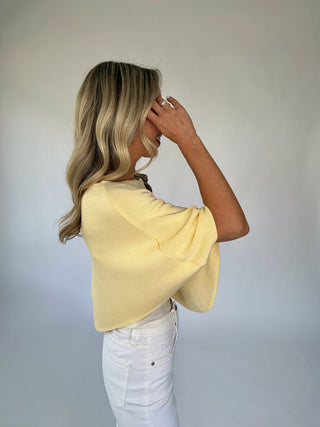 Woman wearing a yellow top and white pants against a plain background