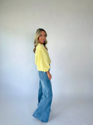 Woman wearing a yellow top and blue jeans against a white background