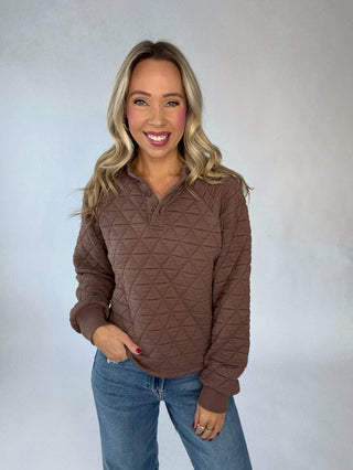 Woman wearing a brown quilted pullover against a plain background