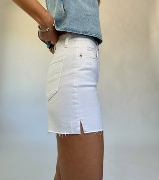 Person wearing a light blue denim shirt and white denim skirt against a plain background