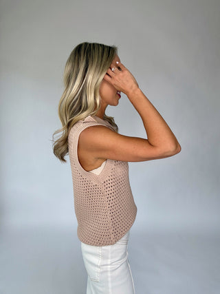Woman wearing a beige crochet sleeveless top against a plain background