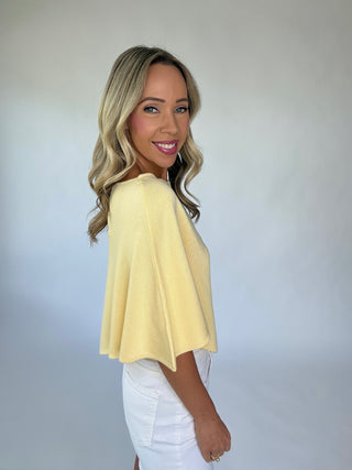 Woman wearing a yellow top and white pants against a plain background