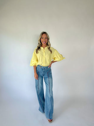 Woman wearing a yellow blouse and blue jeans against a white background