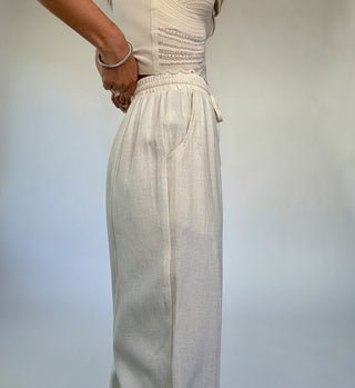Person wearing a light-colored top and pants against a plain background