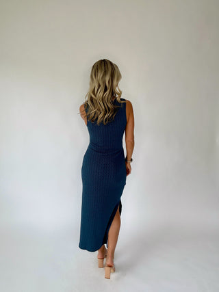 Woman wearing a teal sleeveless dress with a slit on a white background
