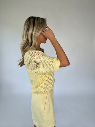 Woman wearing a light yellow crochet top and shorts against a plain background