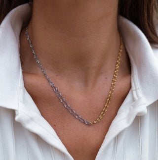 Close-up of a person wearing a gold and silver chain necklace with a white shirt.