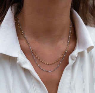 Close-up of a person wearing two gold necklaces on a white shirt.