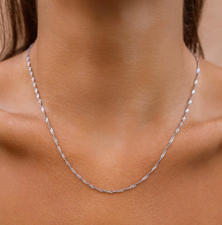 Silver necklace on a person's neck with a neutral background