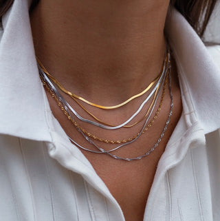 Close-up of a person wearing multiple gold and silver necklaces on a white shirt.
