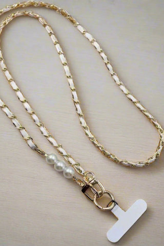 Gold chain necklace with pearl accents and a white tag on a beige background