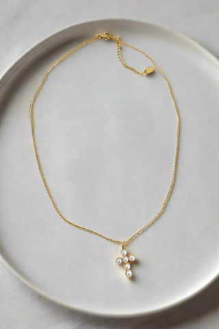 Gold necklace with a pearl pendant on a light gray plate