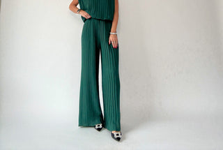 Person wearing a green pleated jumpsuit on a plain background
