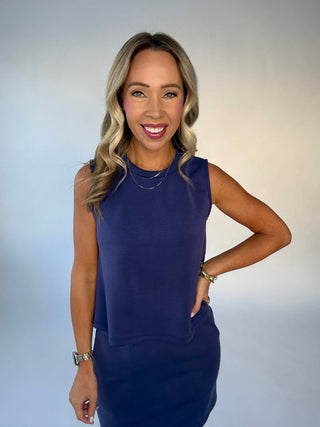 Woman wearing a blue sleeveless top and skirt against a plain background