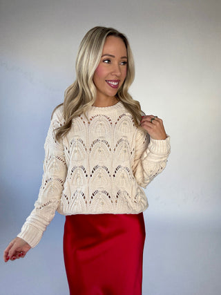 Woman wearing a cream lace sweater and red skirt against a plain background