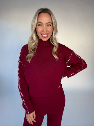 Woman wearing a maroon outfit with white accents on a plain background