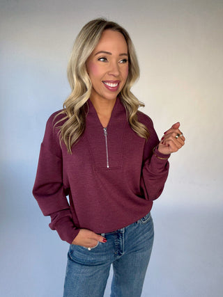 Woman wearing a maroon zip-up sweatshirt and blue jeans against a plain background