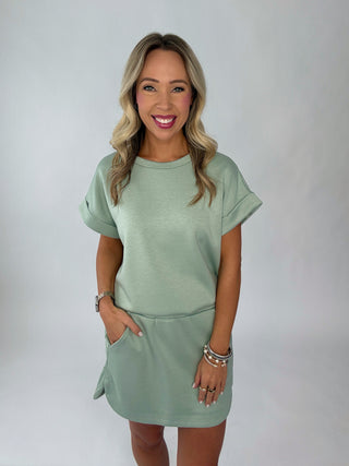 Woman wearing a sage green dress against a plain background