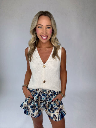 Woman wearing a white sleeveless top and patterned shorts against a plain background